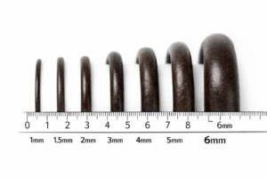 Leather cords of varying thickness from 1mm to 6mm arranged in ascending order above a measuring scale, showing size differences and texture on a clean background.