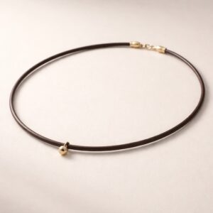 Minimalist round leather cord necklace with a small gold bead pendant, placed on a clean neutral background with soft lighting