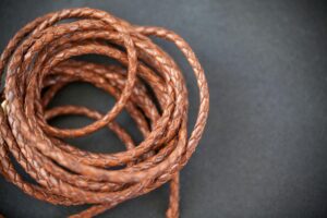 Coiled braided leather cord in brown on a dark background.