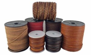 Collection of genuine leather cords and straps in multiple colors including brown, tan, black, and red, displayed on large spools for jewellery making and crafting.