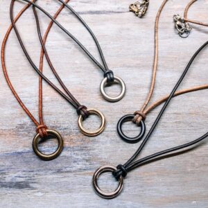 Stylish leather cord necklaces in black, brown, and tan colors with metal ring pendants displayed on a wooden background.