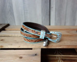 Handcrafted custom leather belts USA made with carved western pattern, turquoise border, and silver buckle on rustic wood.